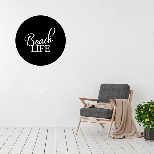Beach Life coastal typography metal wall art displayed above a modern accent chair, featuring elegant script lettering inside a circular laser-cut steel design.