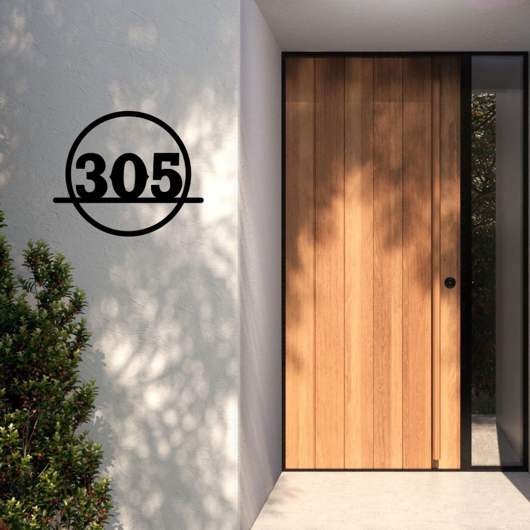 Circular metal house number sign installed on a modern rendered entrance wall beside a contemporary timber front door.