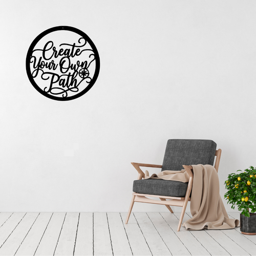 Create Your Own Path | Inspirational Metal Wall Art displayed on a modern living room wall above a grey accent chair, featuring elegant script typography with a compass design in a circular black metal frame.