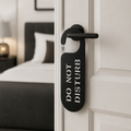 Modern black metal "Do Not Disturb" door hanger sign displayed on a bedroom door handle in a contemporary interior.