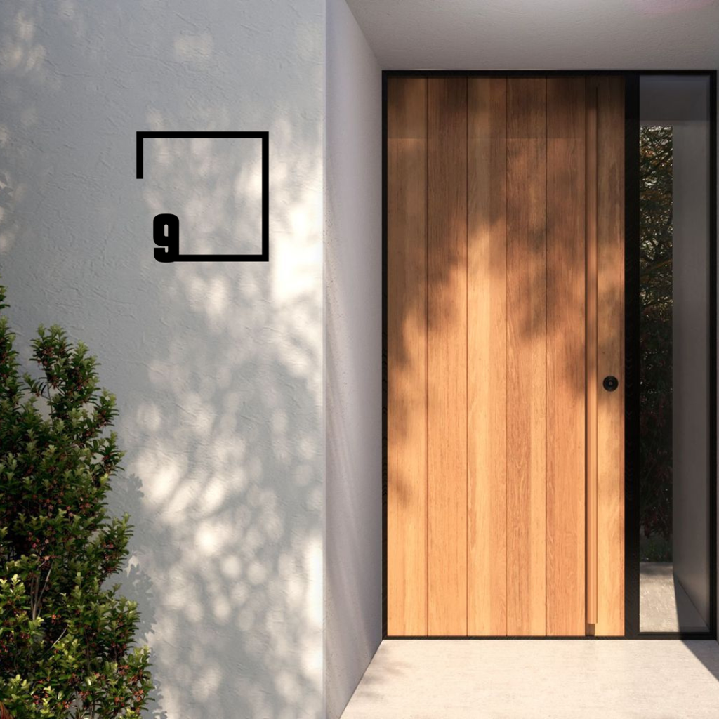 FrameLine custom metal house number installed on a modern rendered entrance wall beside a timber front door.