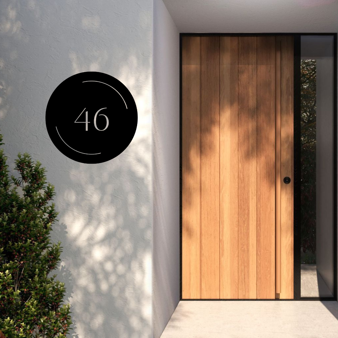 Halo Arc modern circular house number installed on a rendered entrance wall beside a contemporary timber front door.