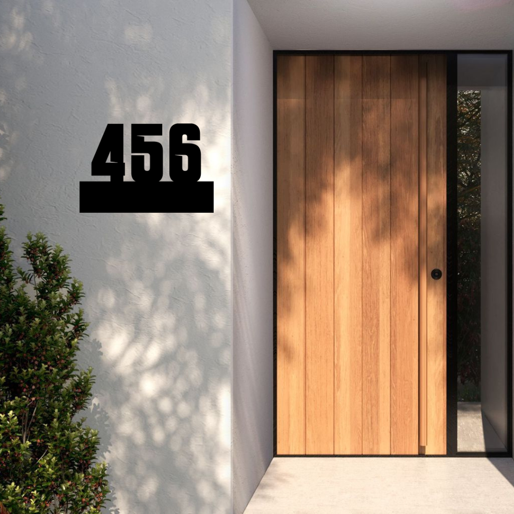 Industrial floating metal house number sign installed on a contemporary rendered entrance wall beside a modern timber front door.