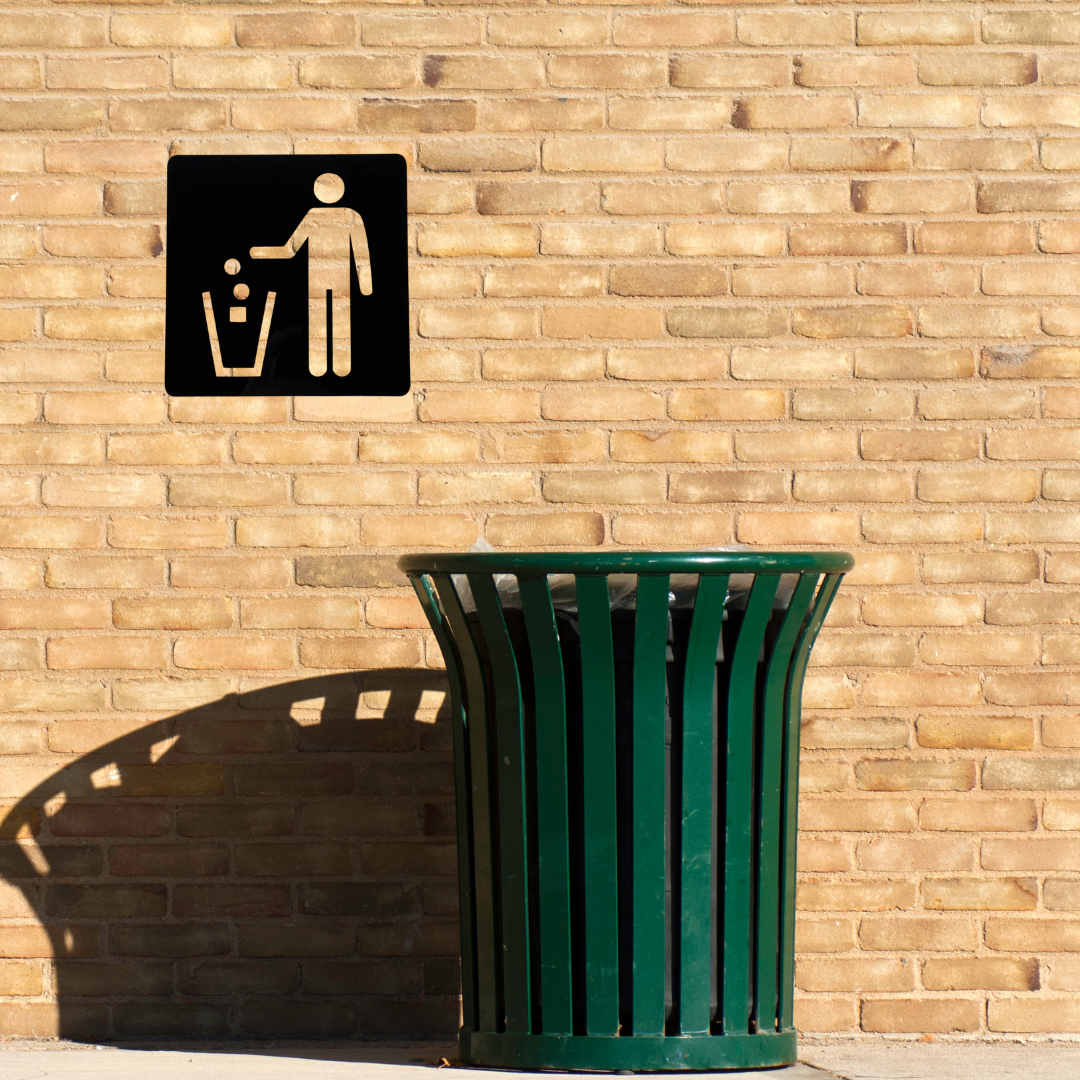 Keep It Clean Litter Bin Metal Sign mounted on an outdoor brick wall above a public waste bin.