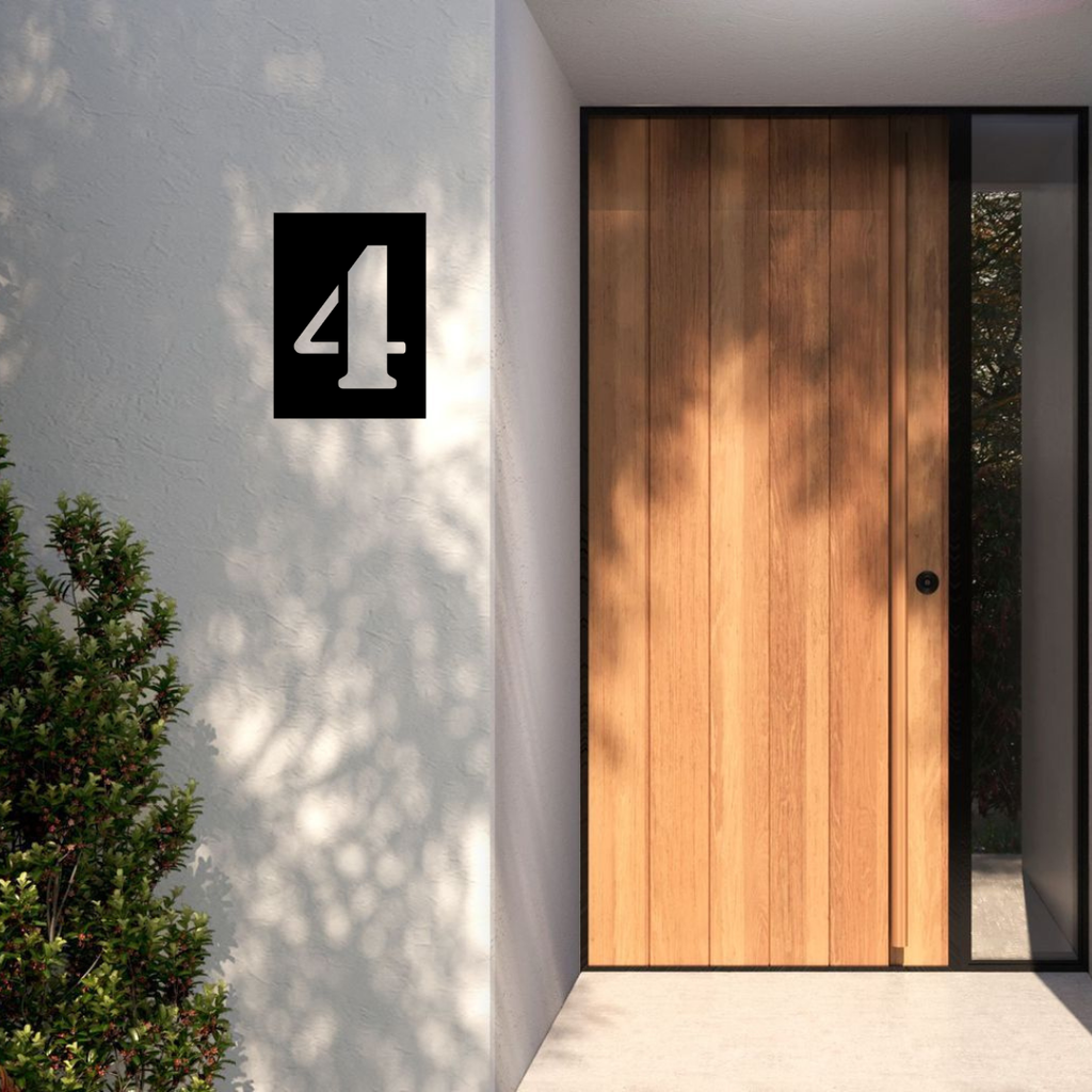 Modern split stencil metal house number installed on a rendered exterior wall beside a contemporary timber entrance door.