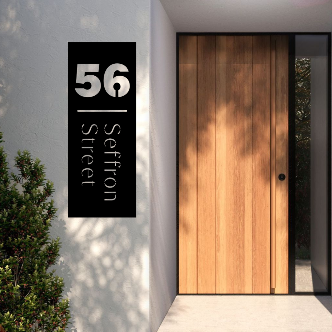 Modern vertical house number and street name sign installed beside a contemporary timber front door on a rendered entrance wall.