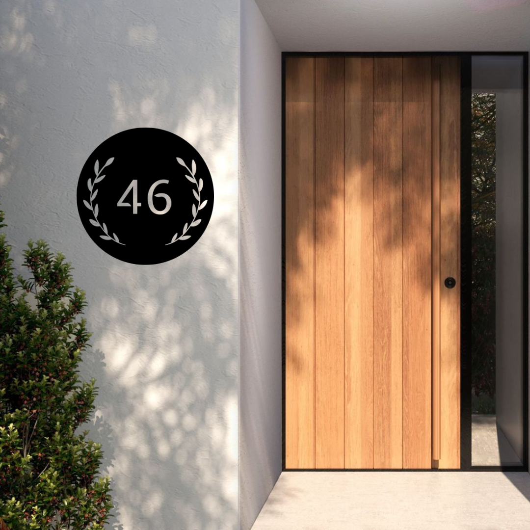 Heritage Round custom circular metal house number mounted on a modern rendered entrance wall beside a timber front door.