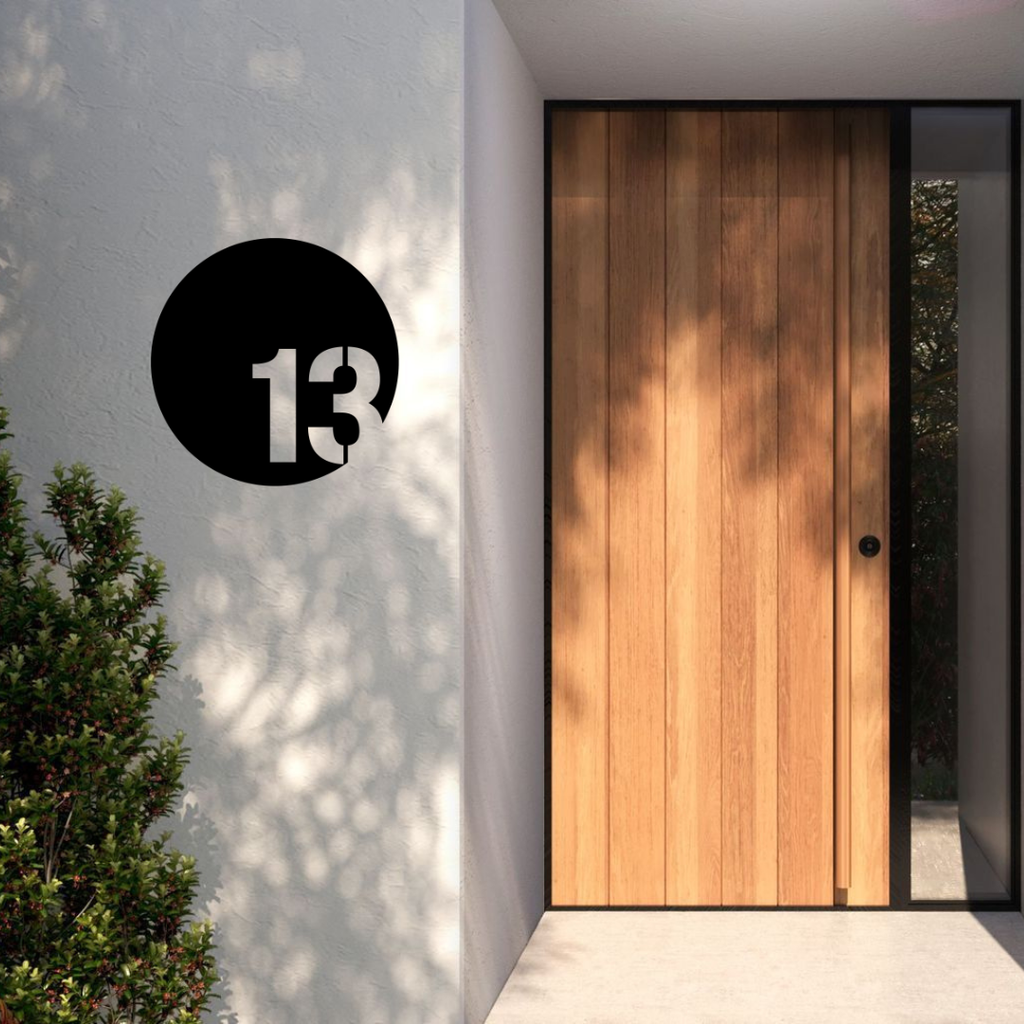 Origin Arc modern circular house number installed on a rendered entrance wall beside a contemporary timber front door.