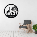Savanna Grace | Giraffe Family Metal Wall Art displayed above a modern grey accent chair, featuring an elegant giraffe and calf beneath an African tree in a circular black metal wall art design inspired by the African savanna.