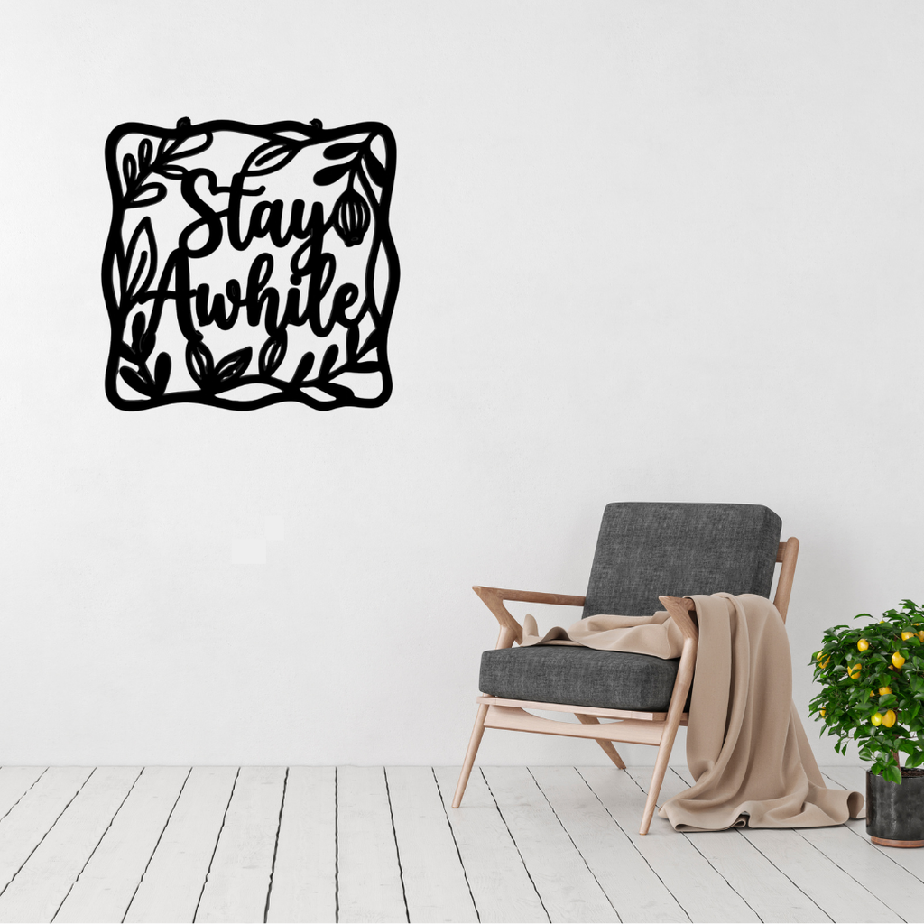 Stay Awhile | Botanical Welcome Metal Wall Art displayed in a bright modern living room, featuring elegant script lettering surrounded by a decorative leafy botanical frame