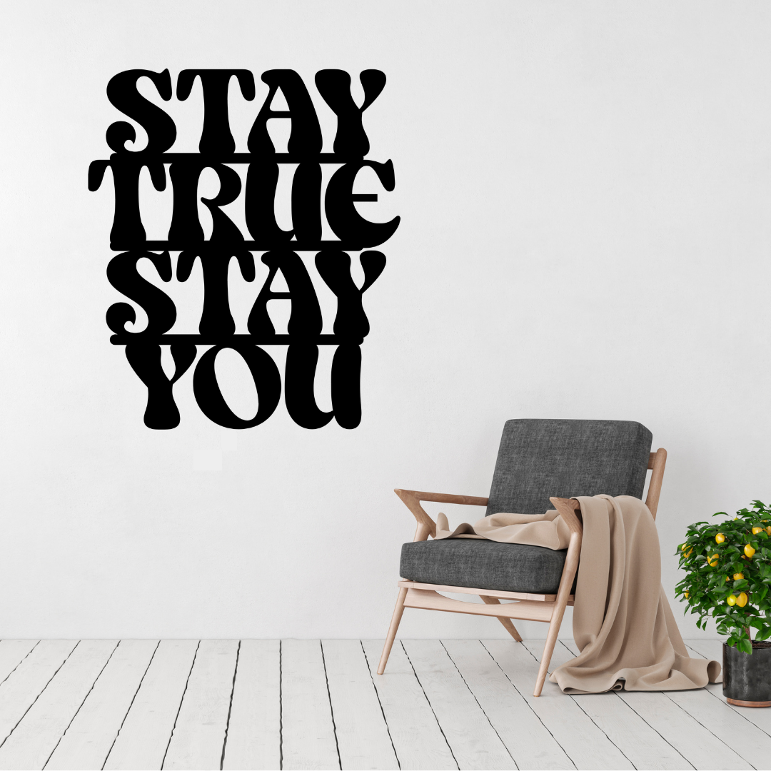 Stay True Stay You inspirational typography metal wall art displayed above a modern accent chair, featuring bold retro lettering laser-cut from premium steel.
