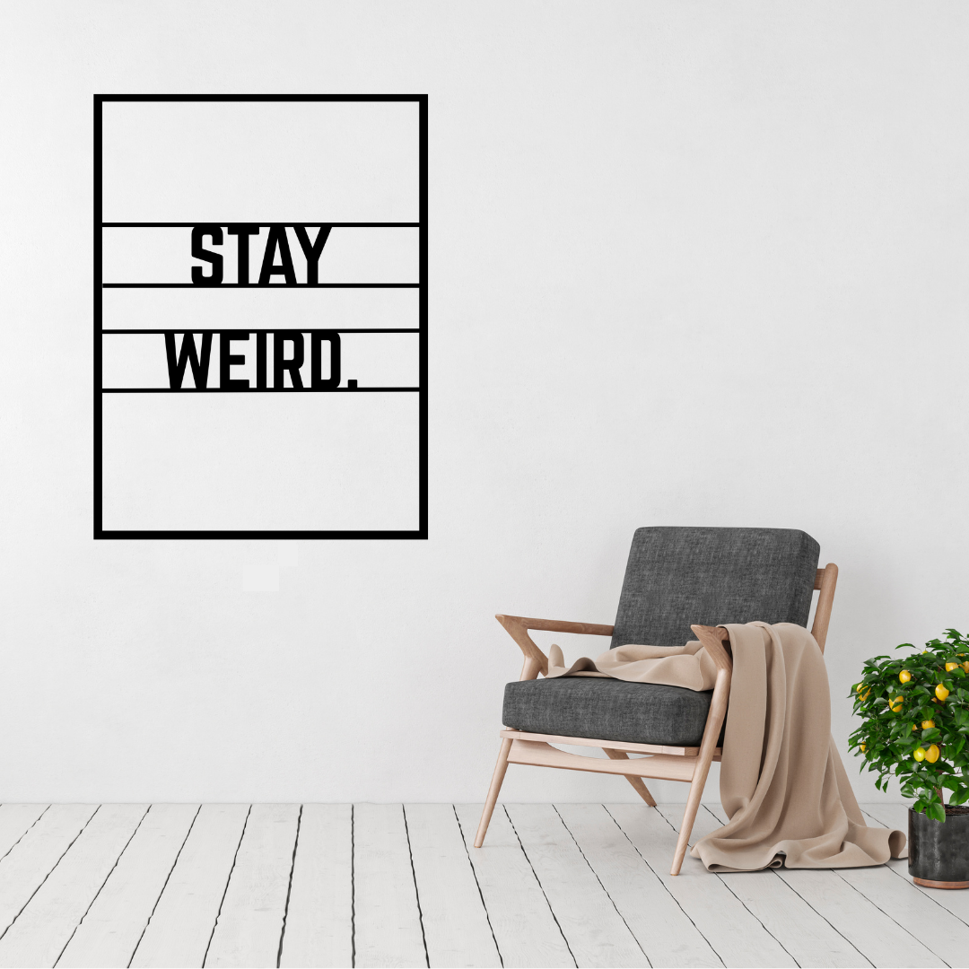 Stay Weird metal wall art displayed above a modern accent chair in a bright contemporary living room.