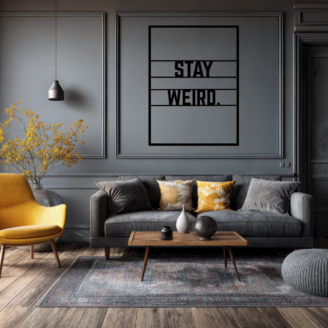 Stay Weird typography metal wall art displayed above a modern sofa in a stylish contemporary living room with dark interior accents.