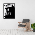 Take It Easy retro typography metal wall art displayed in a modern living room beside a comfortable lounge chair.