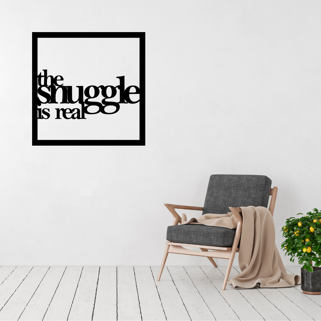 The Snuggle Is Real | Bedroom Quote Metal Wall Art displayed above a contemporary accent chair in a modern living space.