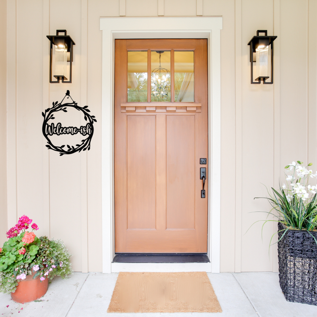 Welcome-ish | Humorous Metal Welcome Sign displayed beside a modern front door, showcasing a stylish leafy wreath with the fun "Welcome-ish" message.
