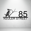 Metal house number sign with perched bird design on a grey background